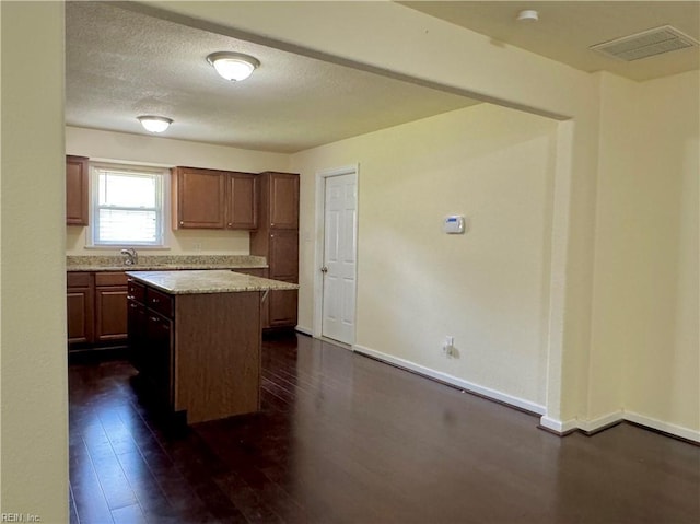 kitchen with a kitchen island, dark wood-style flooring, a sink, baseboards, and visible vents