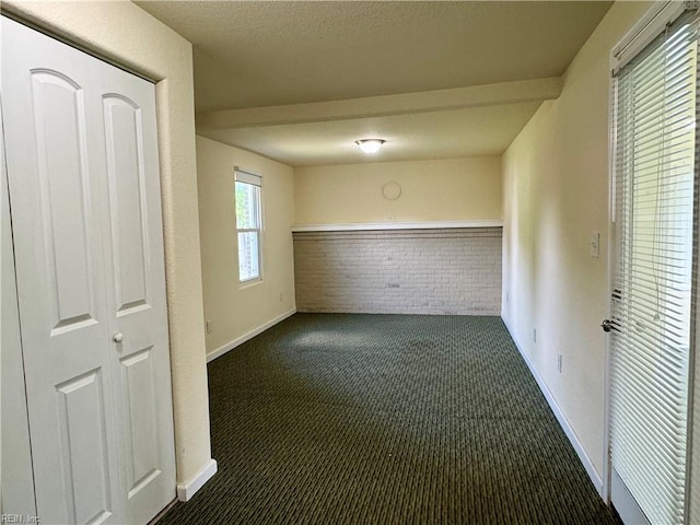 hall with a textured ceiling, dark carpet, brick wall, and baseboards