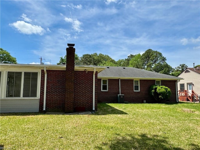 rear view of house with cooling unit, brick siding, a yard, and a chimney