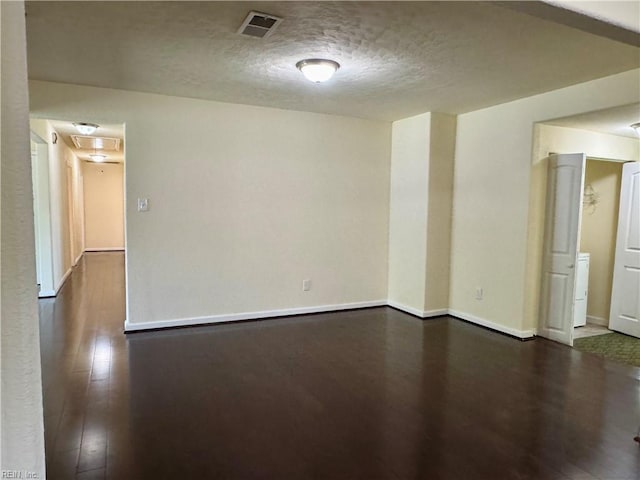 empty room featuring a textured ceiling, wood finished floors, visible vents, and baseboards