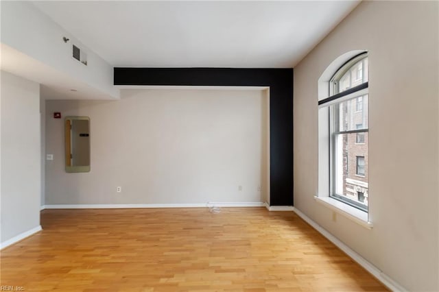 spare room with baseboards, visible vents, light wood-style floors, and electric panel
