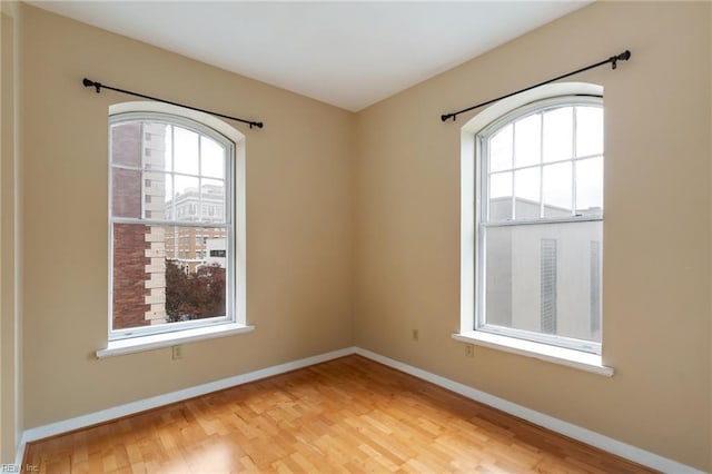 spare room featuring light wood-style floors, plenty of natural light, and baseboards