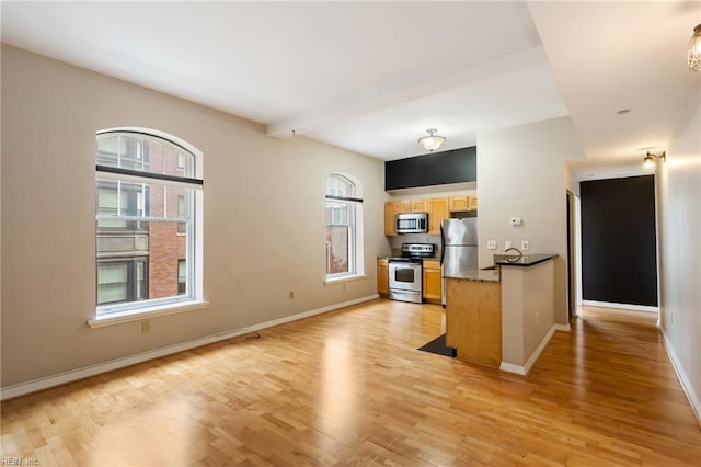 kitchen with baseboards, light wood-type flooring, beam ceiling, and appliances with stainless steel finishes