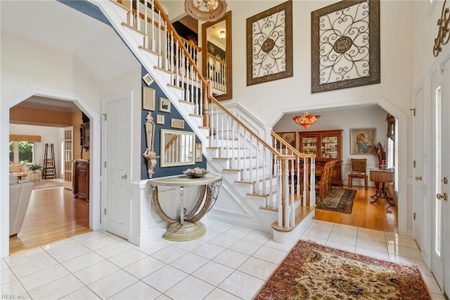 entryway with stairway, arched walkways, tile patterned flooring, and a towering ceiling