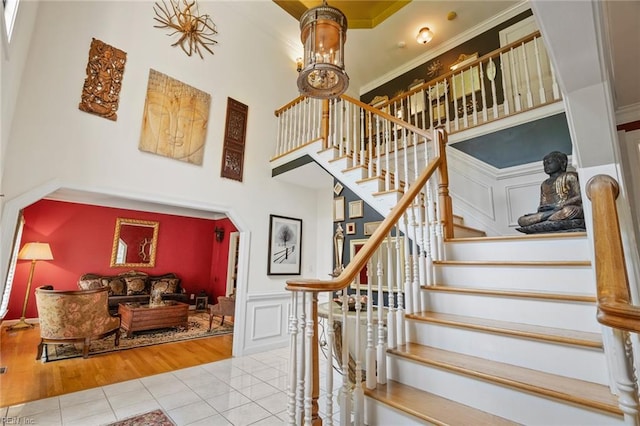 stairs with wainscoting, a high ceiling, tile patterned floors, ornamental molding, and a decorative wall