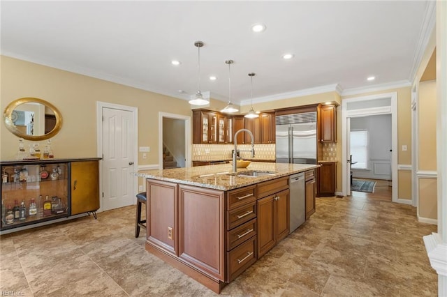 kitchen featuring brown cabinetry, backsplash, appliances with stainless steel finishes, a center island with sink, and a sink