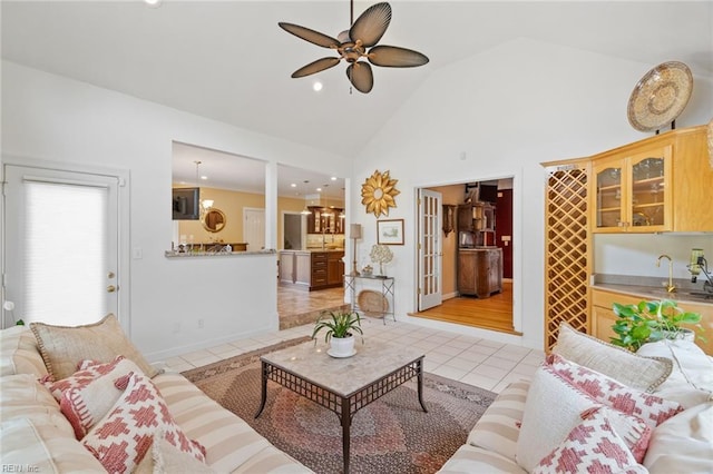 living area with bar, a ceiling fan, light tile patterned floors, high vaulted ceiling, and baseboards