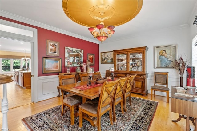 dining space with an inviting chandelier, light wood-style floors, crown molding, and a wainscoted wall