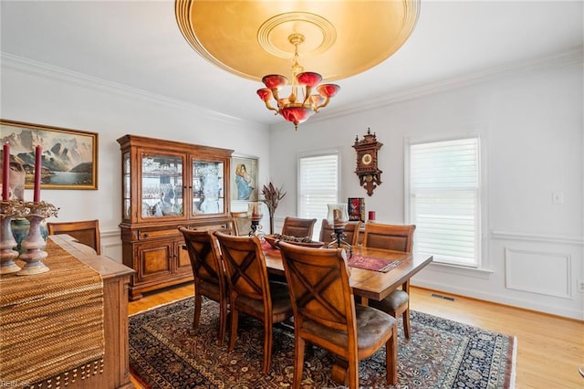dining area with crown molding, light wood-style flooring, a chandelier, and visible vents