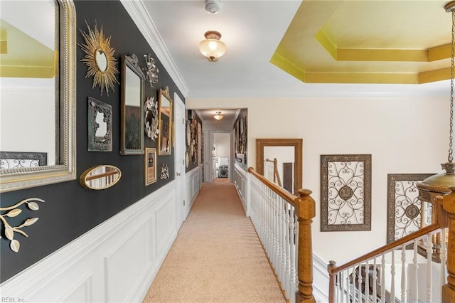 hallway with wainscoting, light carpet, a decorative wall, an upstairs landing, and ornamental molding