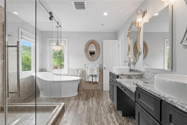full bath with a freestanding bath, wainscoting, tile walls, two vanities, and visible vents
