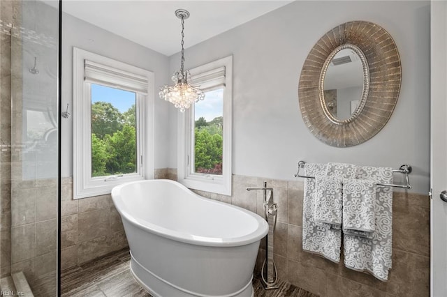 bathroom featuring a freestanding tub, tile walls, an inviting chandelier, and a wainscoted wall