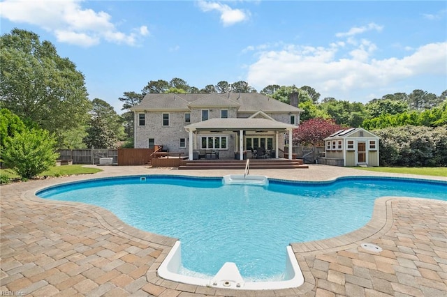 view of pool with fence, a wooden deck, a patio, a fenced in pool, and an outbuilding