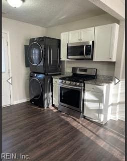 kitchen with stacked washer and dryer, stainless steel appliances, white cabinets, and dark wood-type flooring