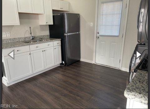 kitchen with a sink, dark wood-type flooring, light stone counters, white cabinets, and freestanding refrigerator
