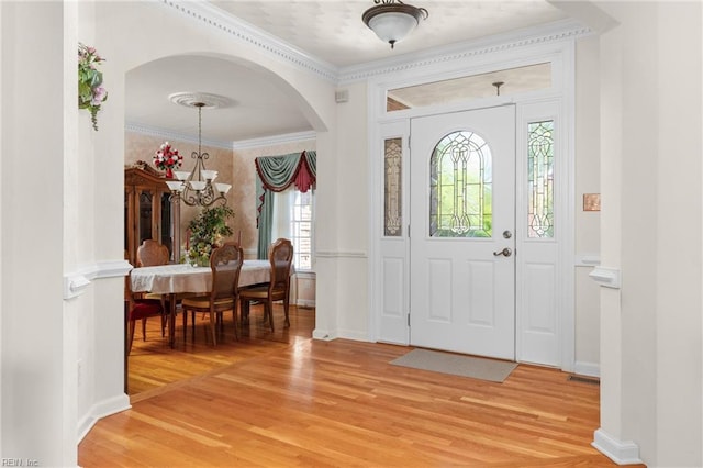 entrance foyer with ornamental molding, a healthy amount of sunlight, arched walkways, and light wood-style flooring