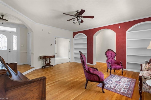 sitting room featuring baseboards, arched walkways, wood finished floors, a ceiling fan, and built in shelves