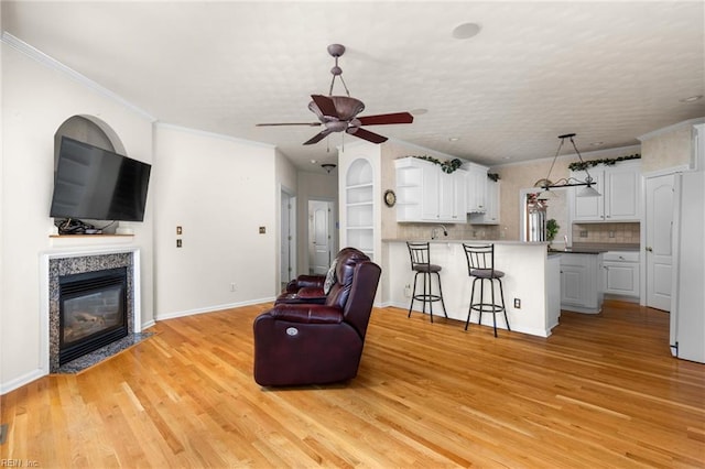 living room with ceiling fan, light wood-style floors, crown molding, and a fireplace