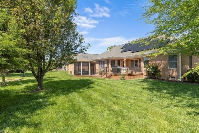 rear view of property with roof mounted solar panels, crawl space, a yard, brick siding, and a sunroom