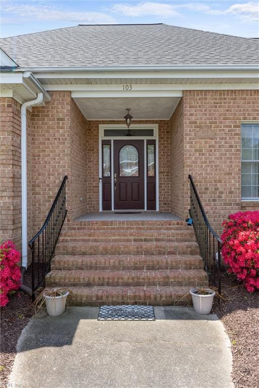property entrance with a shingled roof and brick siding