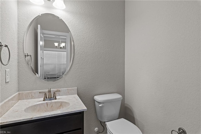 half bath with toilet, a textured wall, and vanity