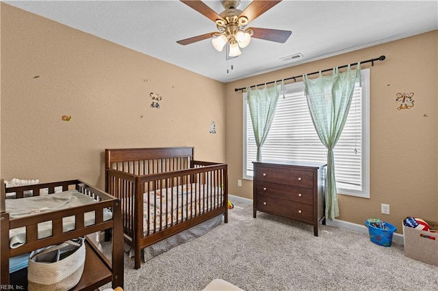 carpeted bedroom with visible vents, a ceiling fan, a nursery area, and baseboards