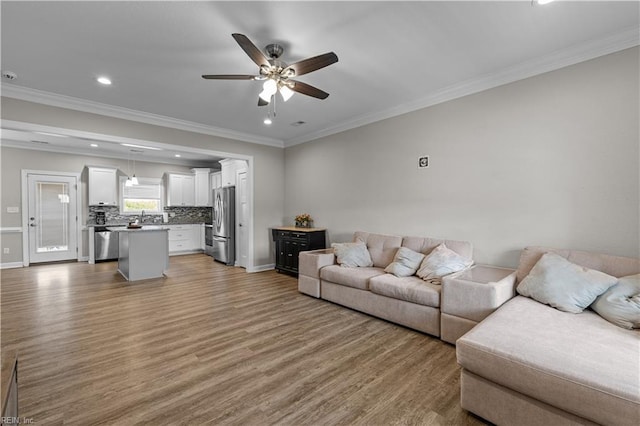 living area with crown molding, baseboards, recessed lighting, light wood finished floors, and a ceiling fan