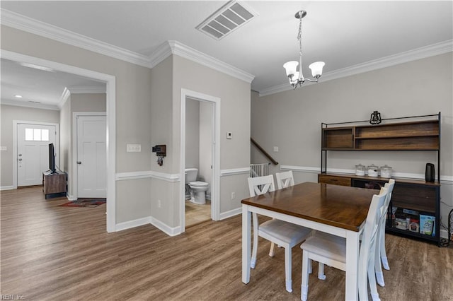 dining area featuring crown molding, an inviting chandelier, visible vents, and wood finished floors