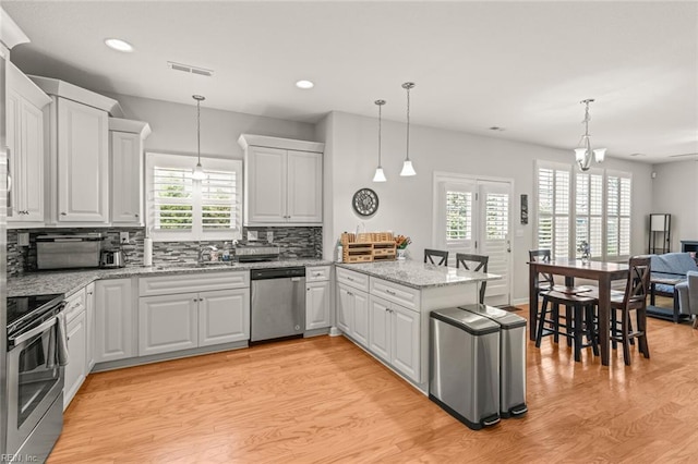 kitchen featuring light wood-style flooring, appliances with stainless steel finishes, backsplash, visible vents, and a peninsula