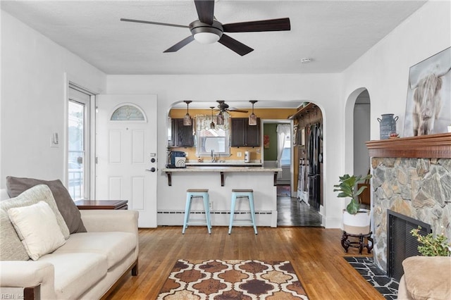 living room featuring arched walkways, a baseboard radiator, a fireplace, a ceiling fan, and dark wood-type flooring