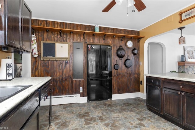 kitchen with stone finish flooring, freestanding refrigerator, dark brown cabinetry, arched walkways, and a ceiling fan