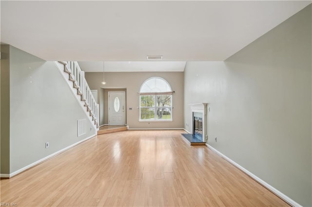 unfurnished living room featuring a fireplace with raised hearth, stairs, visible vents, light wood-style flooring, and baseboards