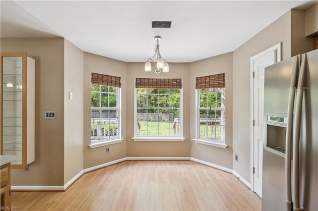 unfurnished dining area with visible vents, a notable chandelier, light wood-style flooring, and baseboards