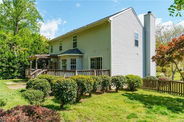 rear view of property featuring a deck, a chimney, a lawn, and a pergola