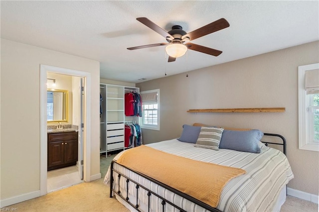 bedroom featuring light colored carpet, a sink, ensuite bath, and baseboards