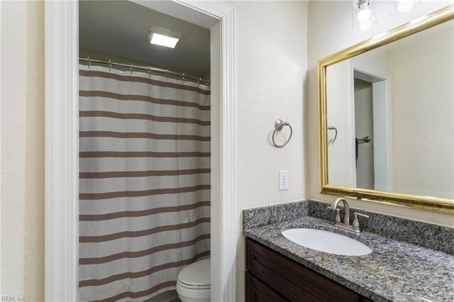 full bathroom with toilet, a shower with curtain, a textured wall, and vanity