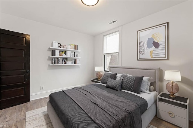 bedroom with baseboards, visible vents, and wood finished floors
