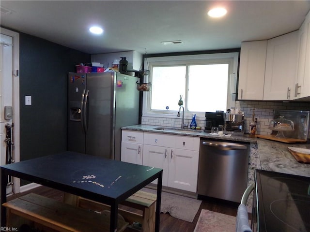kitchen with tasteful backsplash, white cabinets, a sink, stainless steel appliances, and wood finished floors