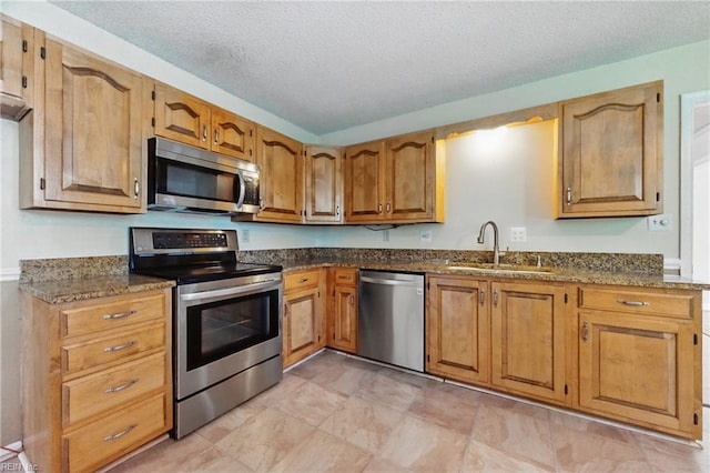 kitchen featuring dark stone counters, stainless steel appliances, brown cabinets, a sink, and a textured ceiling
