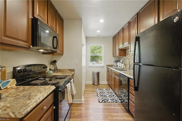 kitchen with decorative backsplash, light wood-style floors, black appliances, a sink, and baseboards