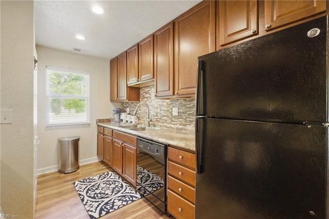 kitchen featuring a sink, decorative backsplash, light wood-style floors, black appliances, and visible vents