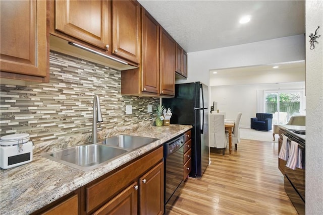 kitchen with tasteful backsplash, black appliances, light wood finished floors, and a sink