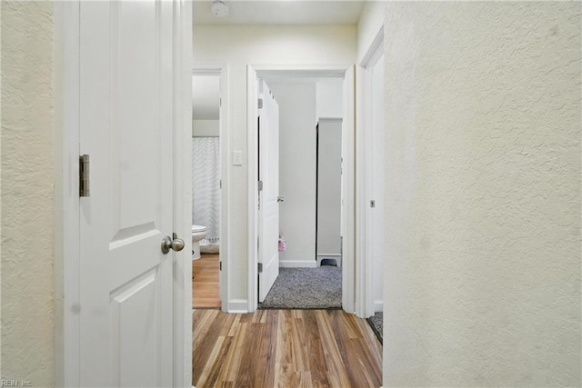 hall featuring baseboards, wood finished floors, and a textured wall