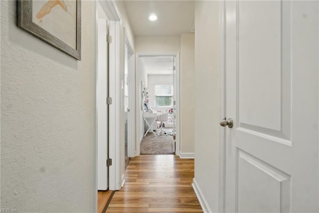 corridor featuring recessed lighting, a textured wall, wood finished floors, and baseboards