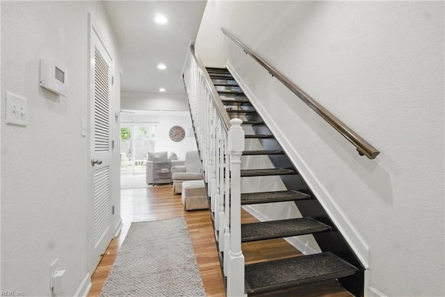 staircase featuring baseboards, recessed lighting, wood finished floors, and a textured wall