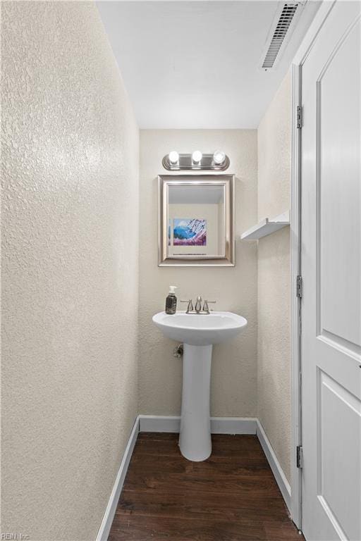 bathroom with wood finished floors, visible vents, a textured wall, and baseboards