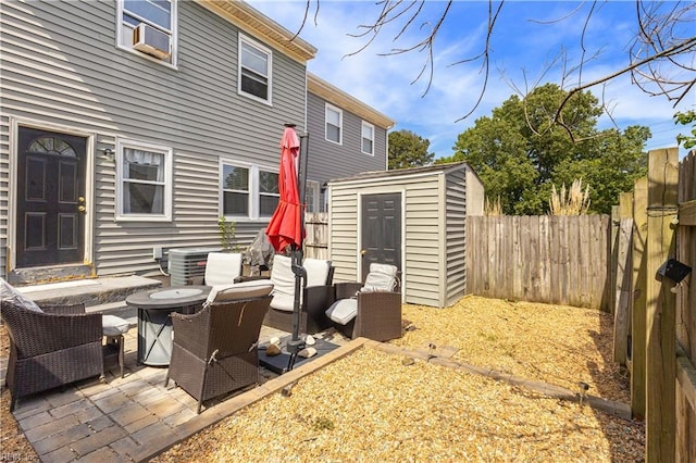 view of patio featuring cooling unit, an outdoor hangout area, a storage unit, an outbuilding, and a fenced backyard