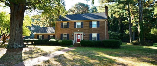 colonial house featuring a chimney, brick siding, and a front yard