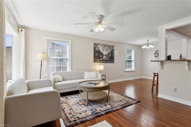 living area featuring a textured ceiling, wood finished floors, baseboards, and ceiling fan with notable chandelier