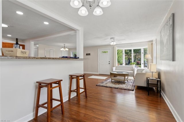 living area featuring dark wood-type flooring, recessed lighting, ceiling fan with notable chandelier, and baseboards